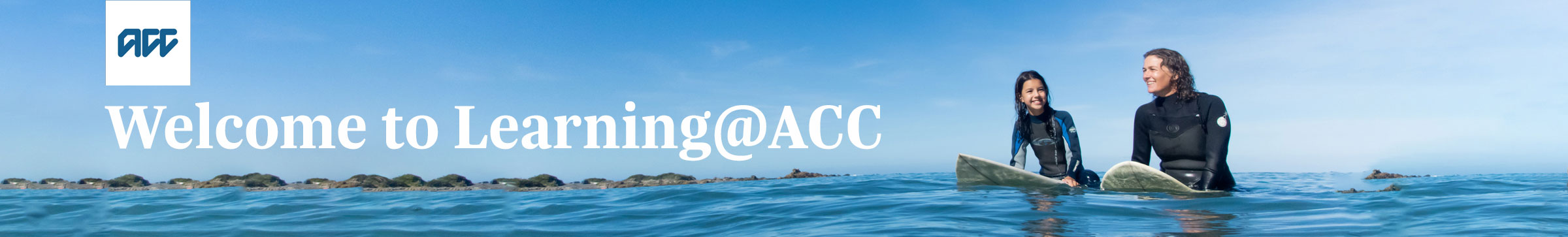 A woman and a young girl sitting on surfboards in the see with hills in the background